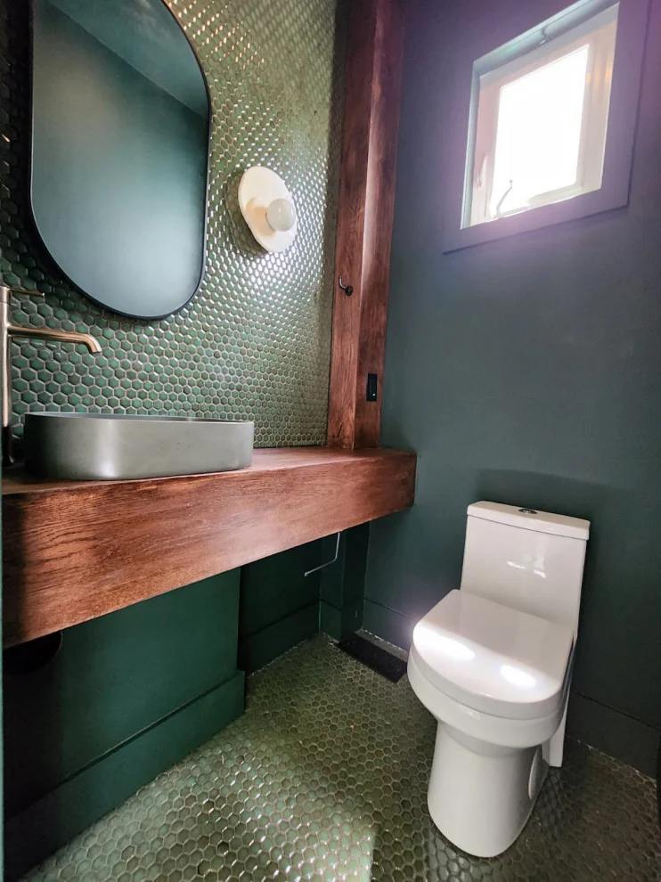 Powder room with green penny tile wall, grey vessel sink on wood counter and pill mirror