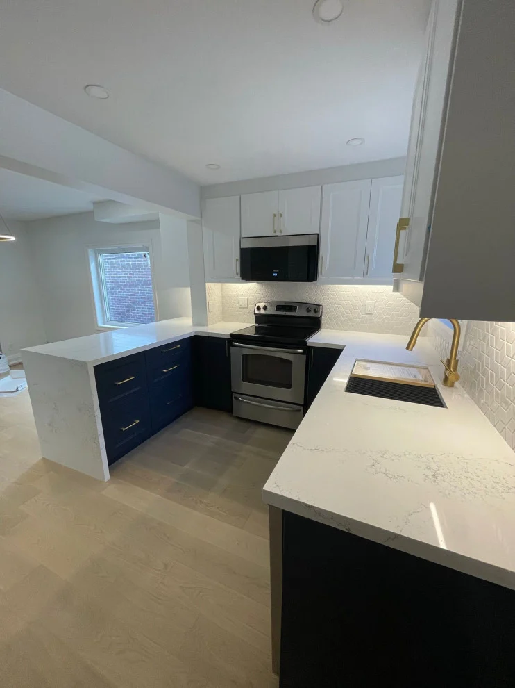 L-shaped kitchen with navy lower cabinets, white quartz waterfall counters and stainless appliances