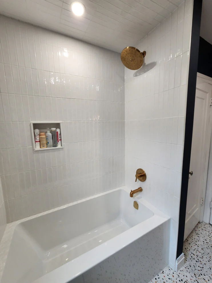 Bathtub alcove with white vertical stacked tile, brushed gold rain shower head and recessed niche