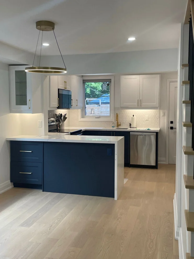 Kitchen with navy peninsula, white uppers, gold ring pendant and light oak flooring