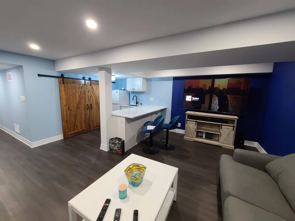 Finished basement with light blue walls, dark plank floor, wet bar, barn door and sectional sofa