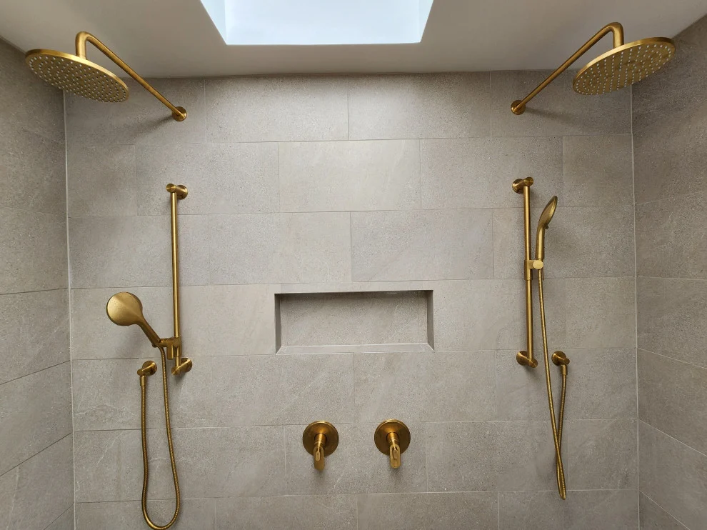Double shower with two brushed gold rain heads, handheld sprayers and long niche in greige tile