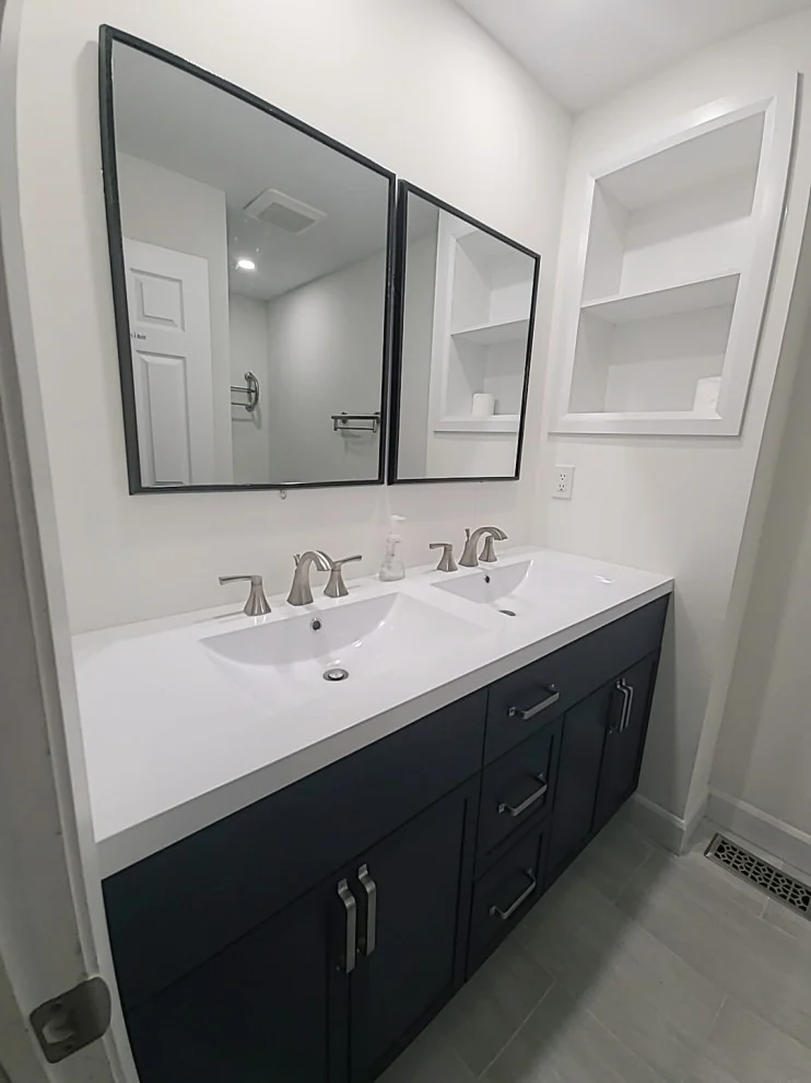 Navy double vanity with white top, brushed nickel faucets, two black framed mirrors and niche shelves