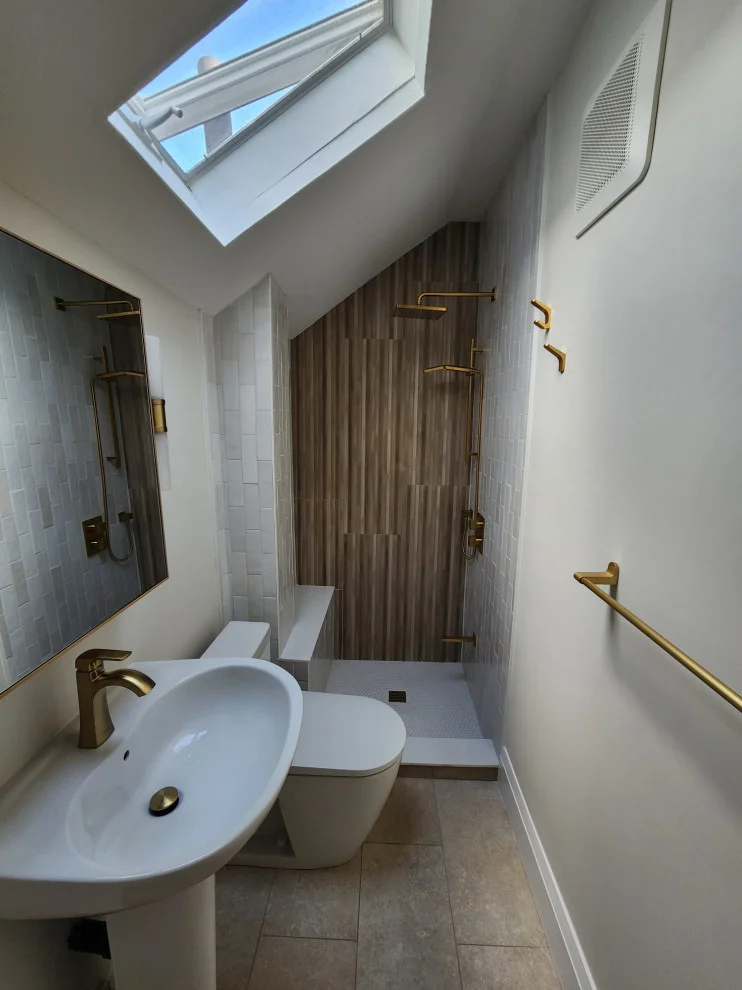 Attic bathroom with skylight, pedestal sink, toilet and shower with wood-grain tile wall