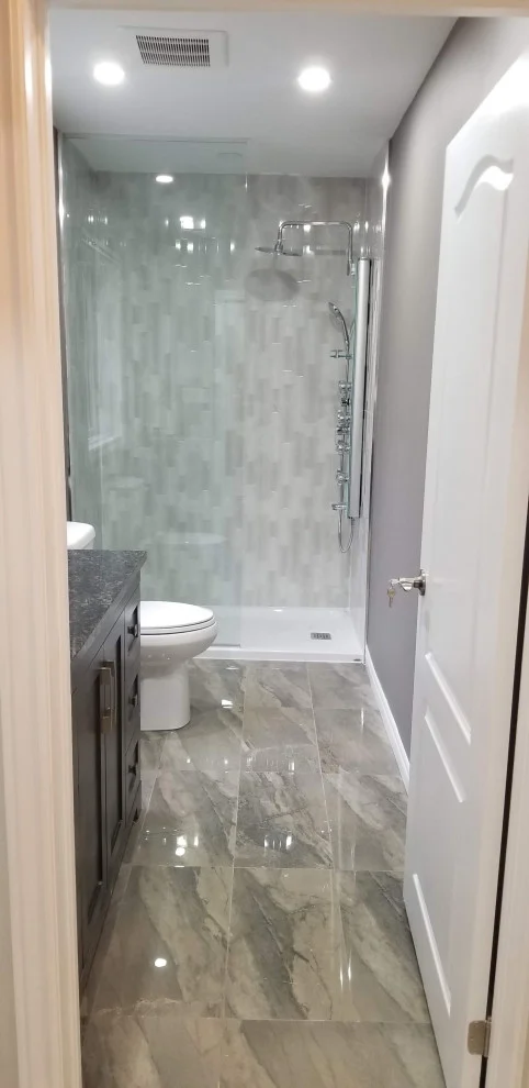 Narrow bathroom with marble-look shower wall, dark vanity and glossy grey marble-look floor tile