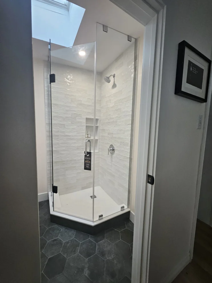 Neo-angle glass shower with white tile, niche and skylight above dark hexagon floor tile