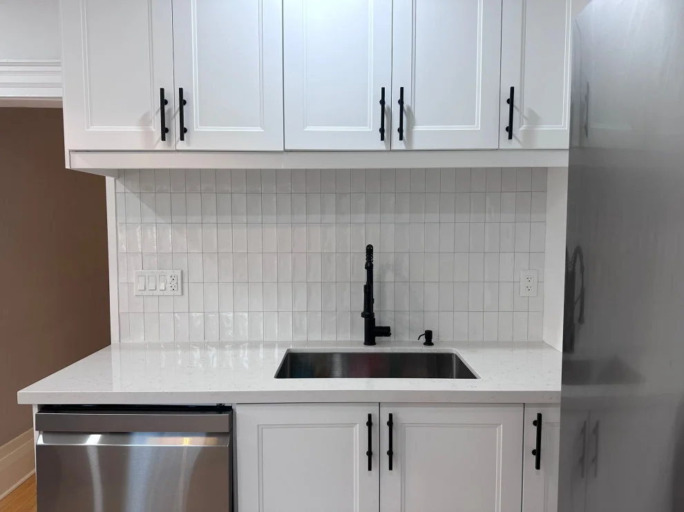 White shaker kitchen with black hardware, white square tile backsplash and black faucet over undermount sink