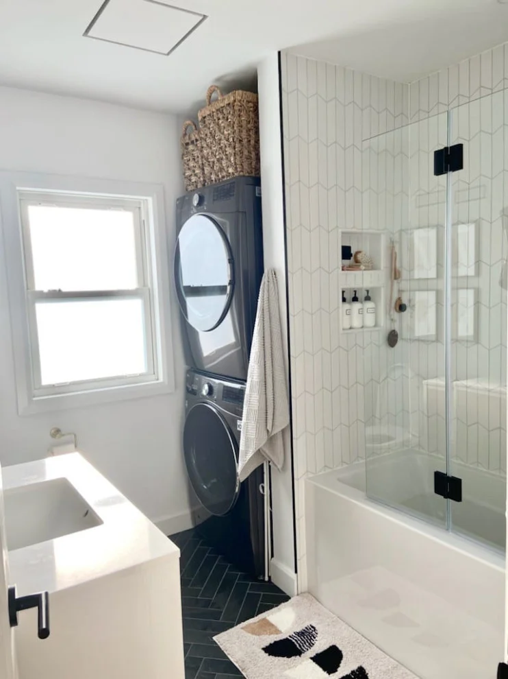 Bright bathroom with stacked washer and dryer, glass tub screen and dark herringbone floor