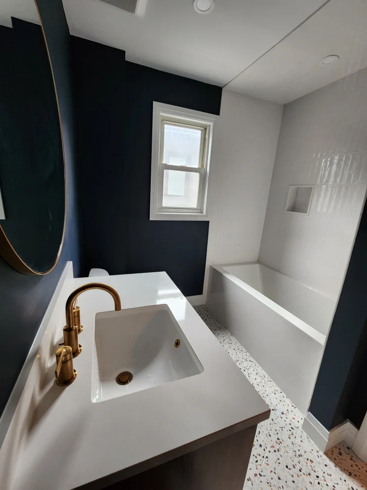 White quartz vanity top with brushed gold faucet, soaker tub and window beyond in renovated bathroom