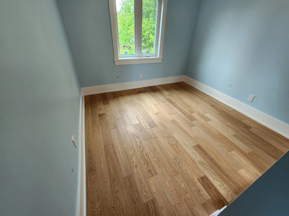 Pale blue bedroom with new light oak hardwood floor, white baseboards and window