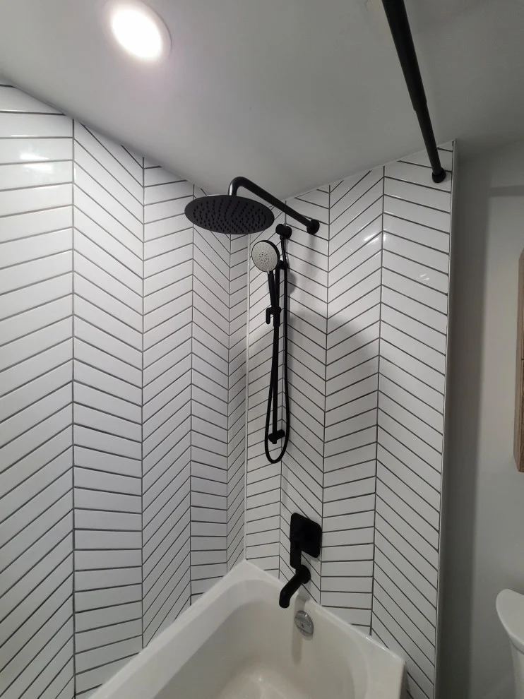 White chevron tile tub surround with matte black rain shower and handheld shower