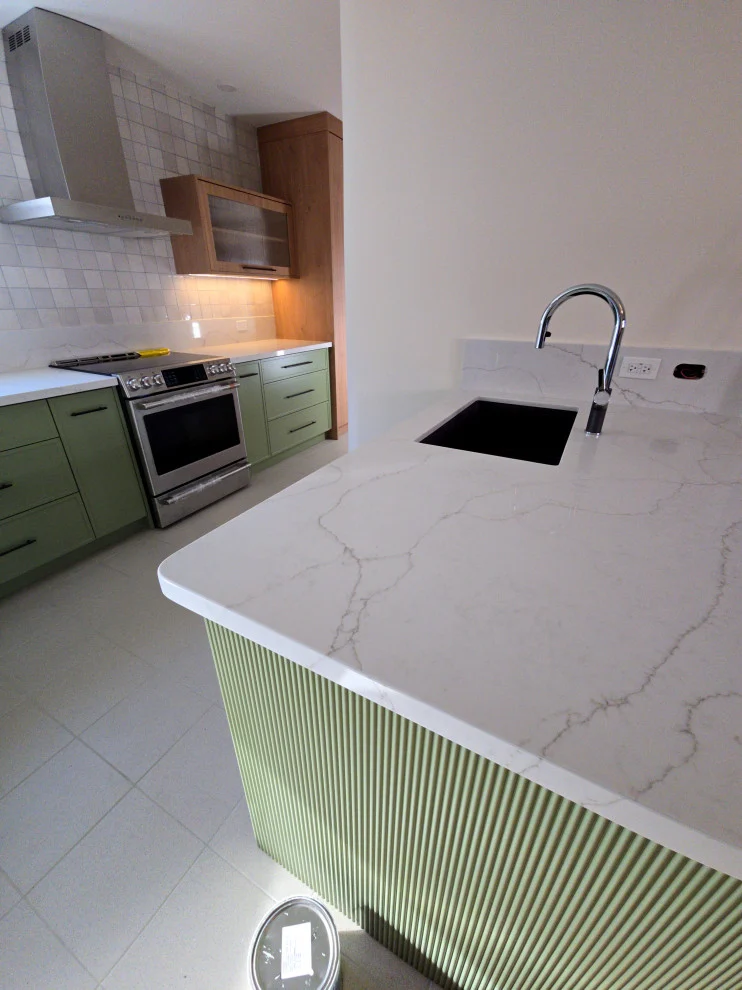 Green fluted island base with white veined quartz top, undermount sink and range wall beyond