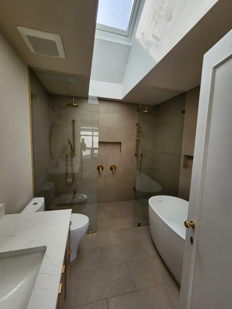 Skylit bathroom with glass walk-in shower, freestanding tub and white vanity counter
