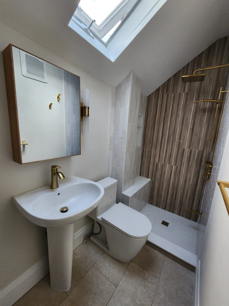Pedestal sink with gold faucet, wood framed mirror cabinet and shower with wood-grain tile