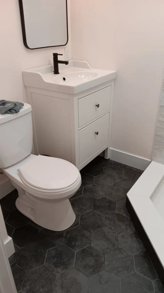 White two-drawer vanity with matte black faucet, black mirror, toilet and charcoal hexagon floor