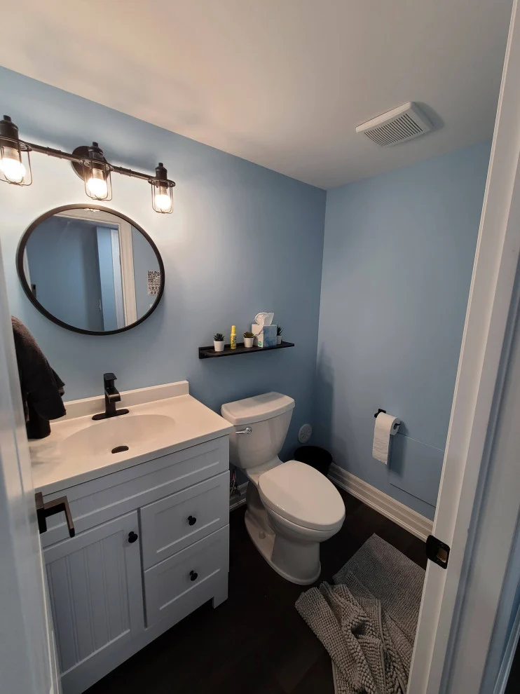 Basement bathroom with light blue walls, white vanity, round black mirror and three-light fixture