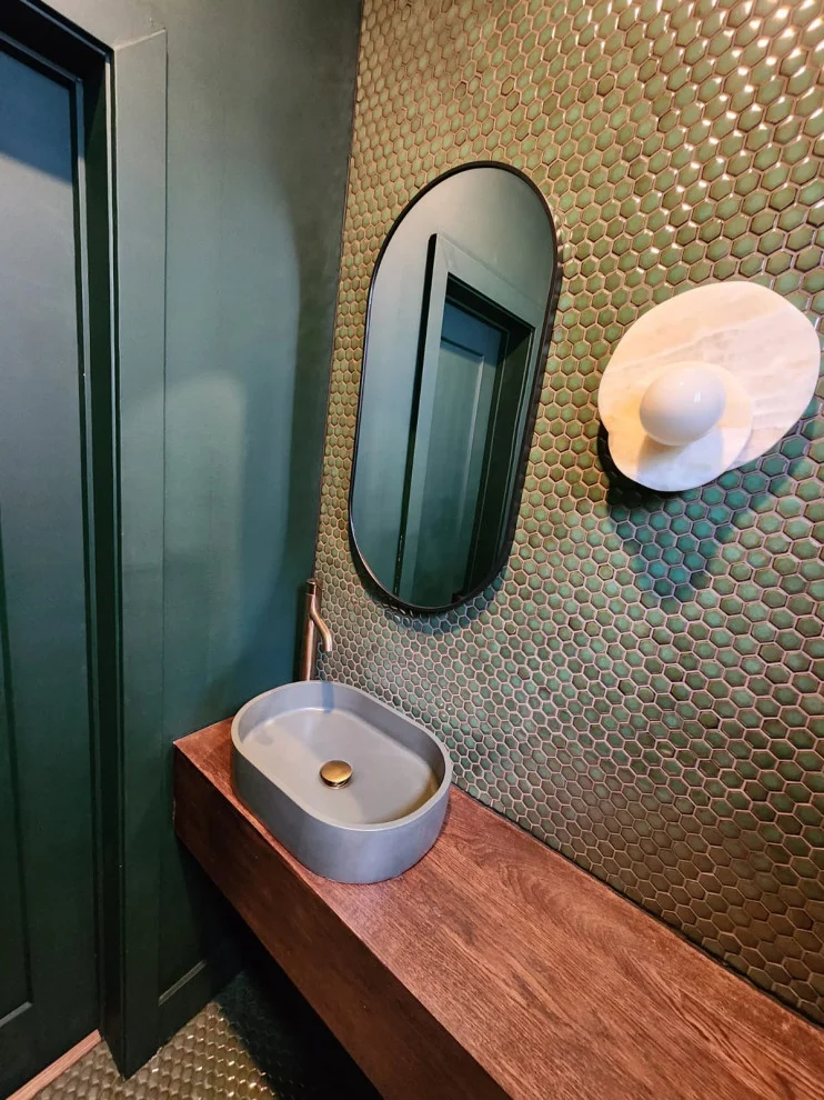 Grey oval vessel sink on wood counter with oval black mirror and penny tile wall