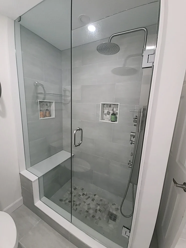 Walk-in glass shower with grey plank tile, bench, rain head, body jets and pebble floor