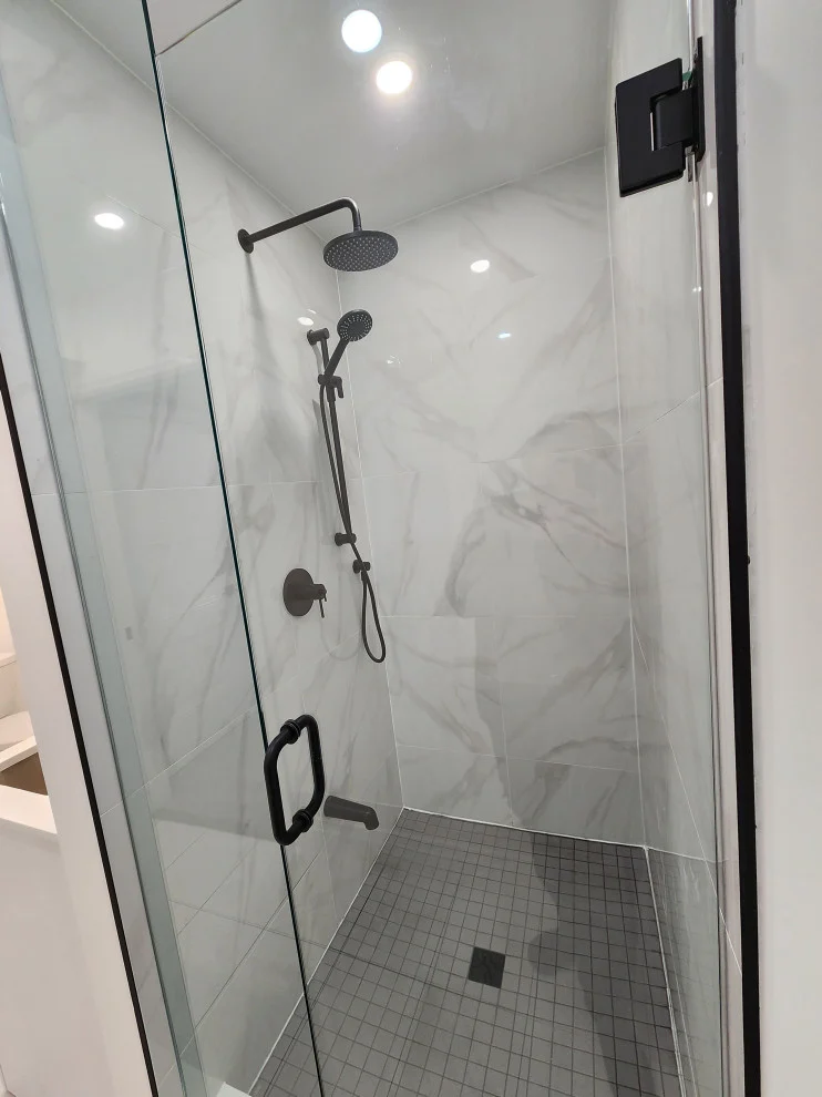 Glass shower with white marble-look tile, matte black rain head and grey mosaic floor