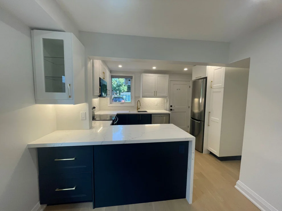 Navy peninsula with white waterfall quartz top, white upper cabinets and stainless fridge