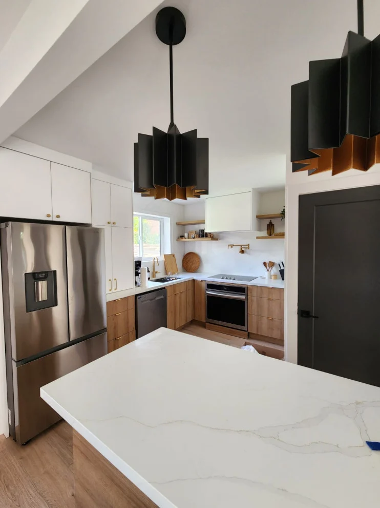Marble-look quartz island with black geometric pendants, stainless fridge and wood lower cabinets