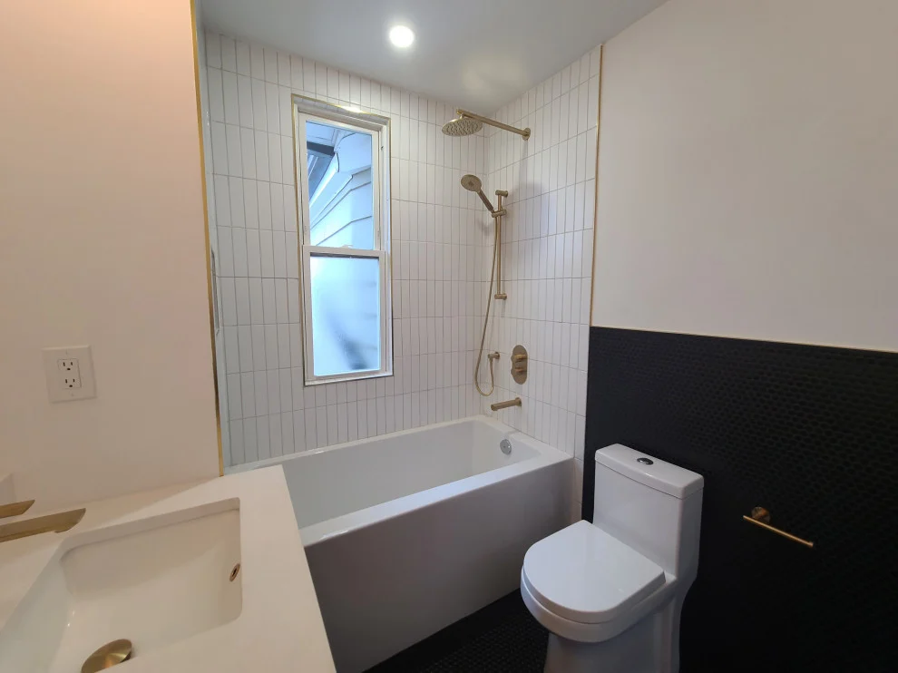 Soaker tub, one-piece toilet and black hexagon wall tile beside white vanity counter