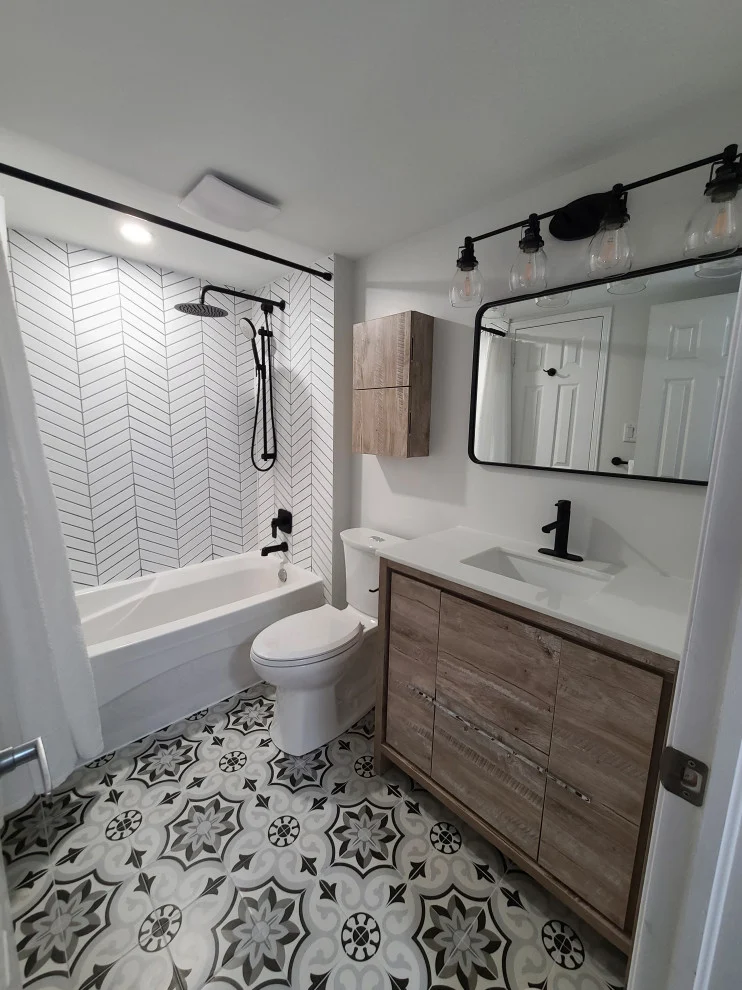 Tub with chevron tile, toilet and wood-look vanity under black framed mirror and globe lights