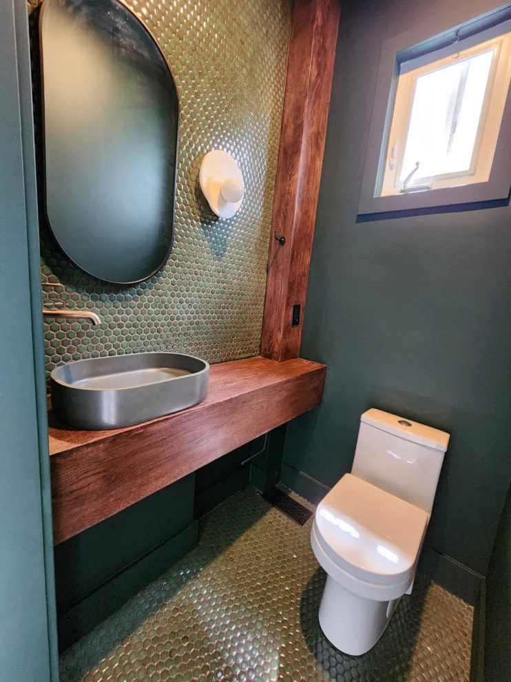 Dark green powder room with floating wood vanity, vessel sink, toilet and small window