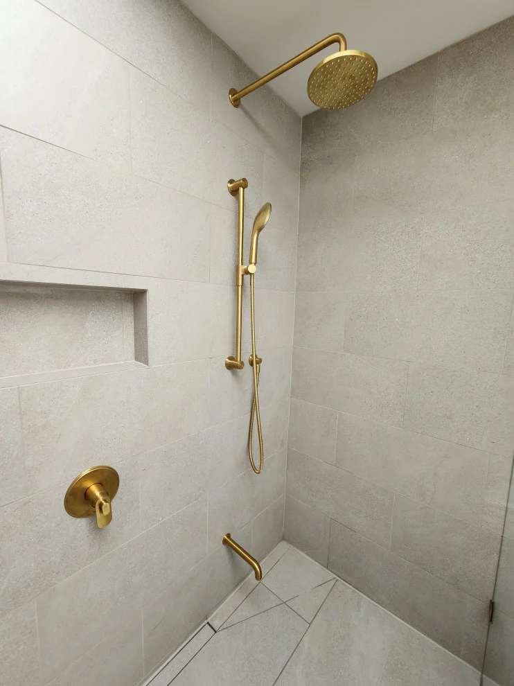 Curbless shower with large-format stone-look tile, gold rain head, slide bar and recessed niche