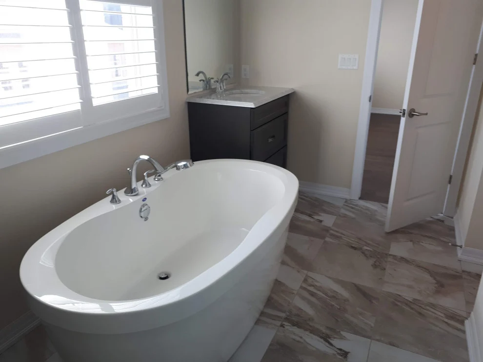 Freestanding white oval tub by a shuttered window with wood-look plank floor tile