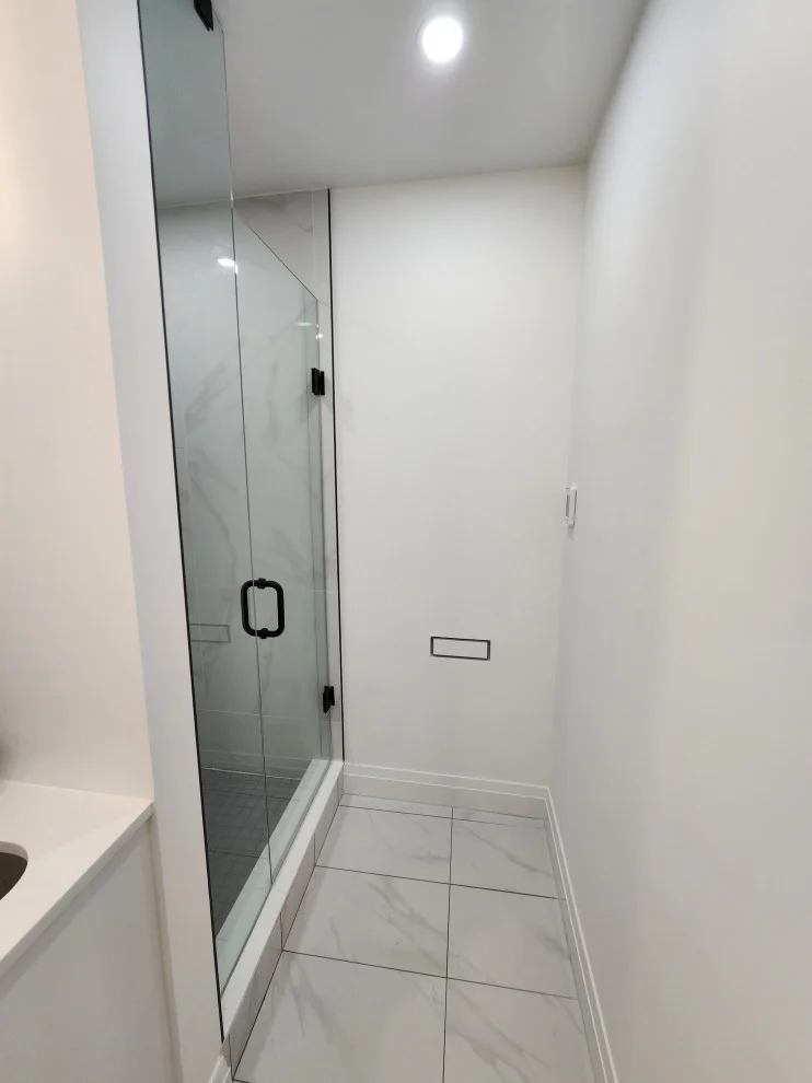 Basement bathroom with frameless glass shower and large marble-look floor tile