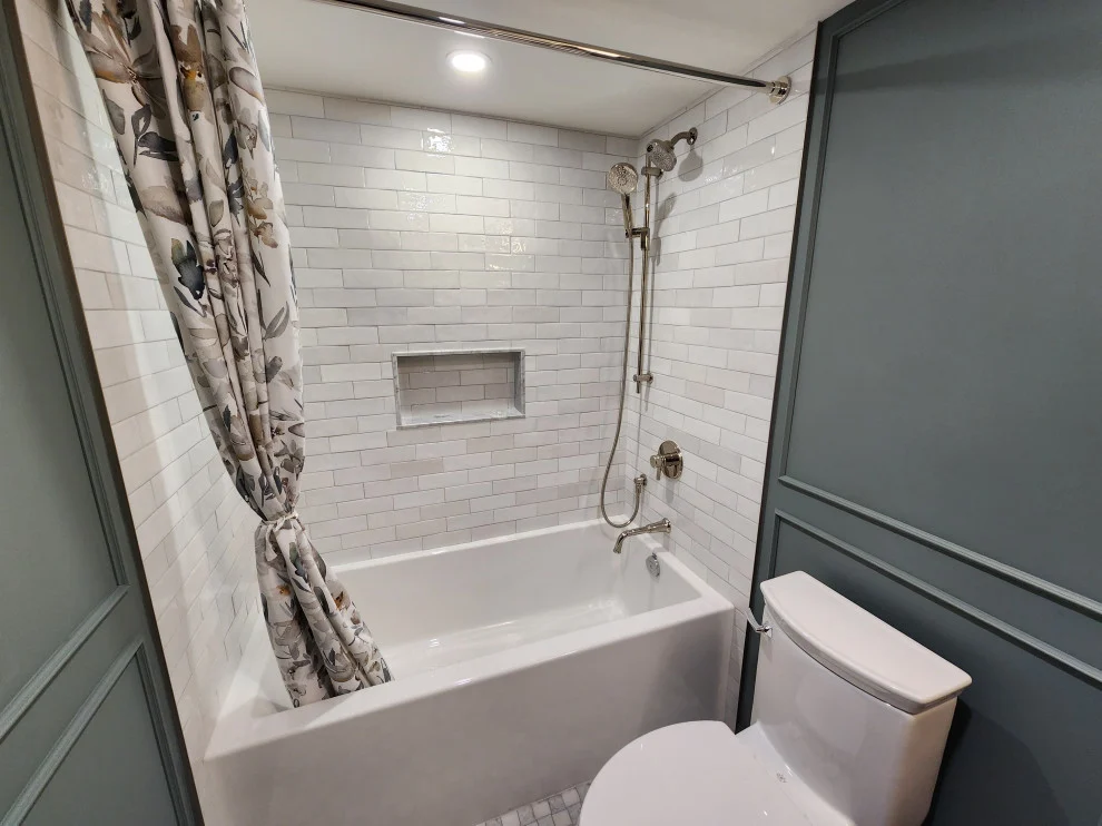 Tub alcove with white subway tile, recessed niche, chrome handheld shower and patterned curtain