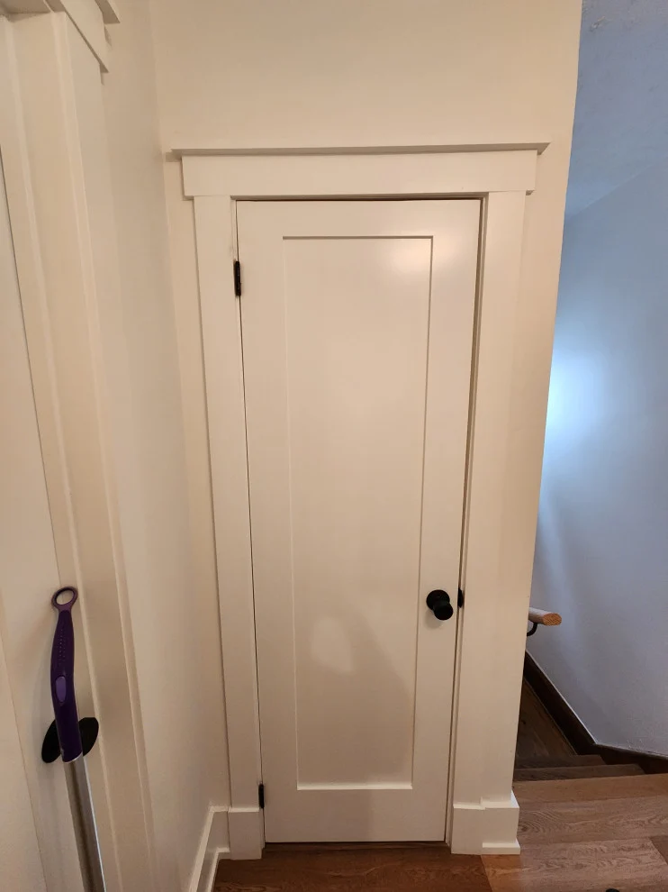 White shaker door and trim at top of stairs with hardwood floor and pale blue walls