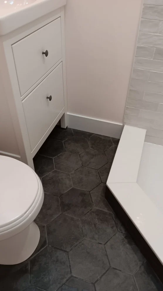 White vanity drawers, toilet and shower curb on large charcoal hexagon floor tile