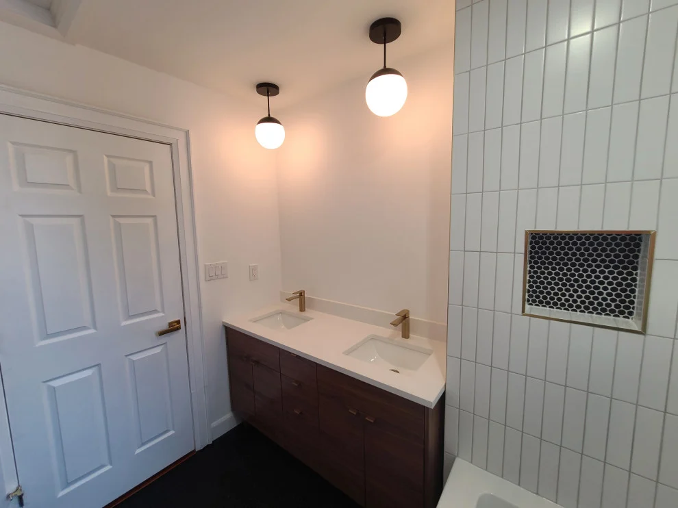 Wood vanity with two gold faucets, globe pendants and niche with black hexagon mosaic