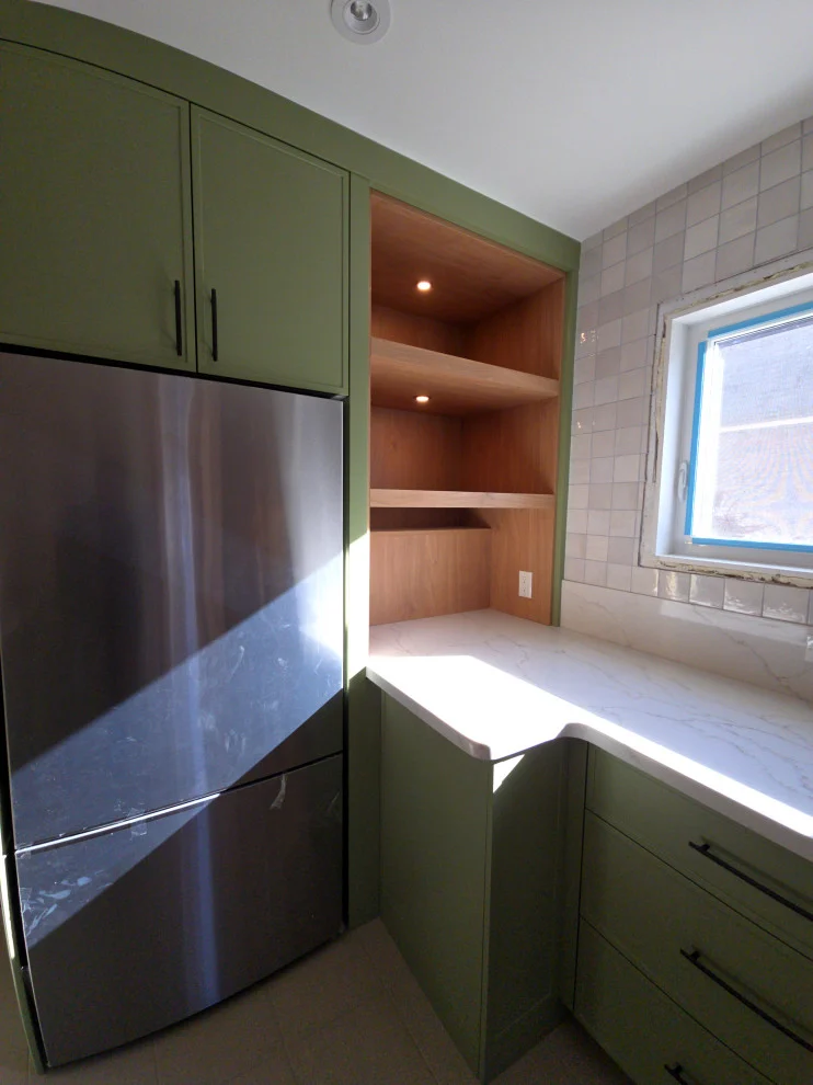 Green cabinetry with built-in stainless fridge, wood open shelves and window corner counter