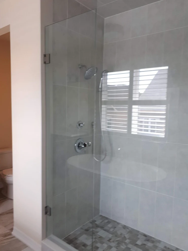 Corner frameless glass shower with grey wall tile, pebble floor and window inside