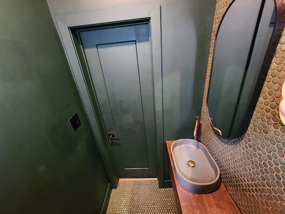Green painted door and walls with vessel sink on wood counter and green penny tile