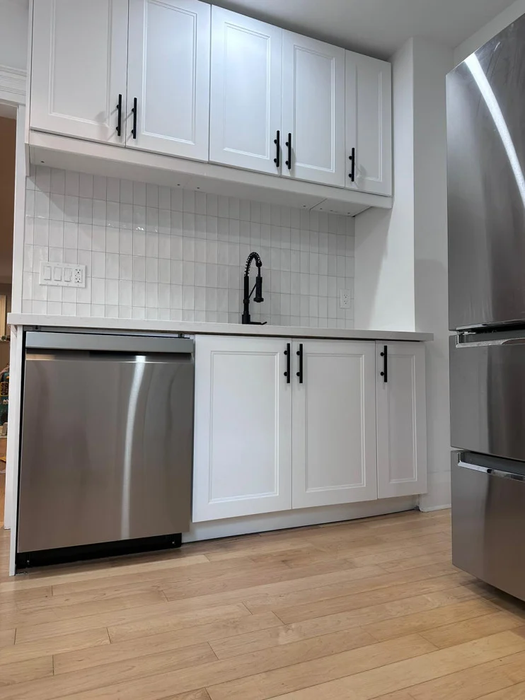 White kitchen wall with stainless dishwasher, black pulls, tile backsplash and hardwood floor