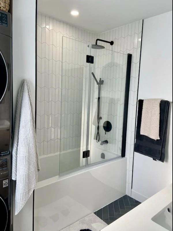 Tub with hinged glass screen, white chevron wall tile and matte black rain shower