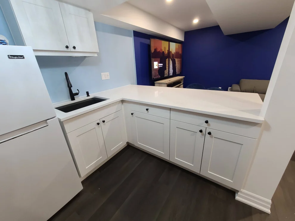 Basement kitchenette with white shaker cabinets, white counter, black faucet and navy accent wall