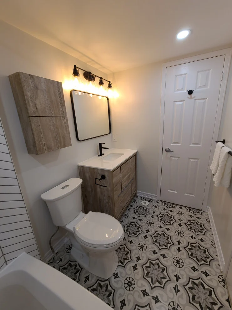Toilet, small wood-look vanity and wall cabinet beside a white door on patterned tile