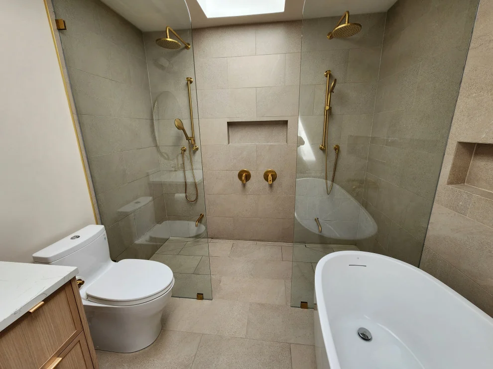 Glass-enclosed double shower behind freestanding tub with skylight and wood vanity edge