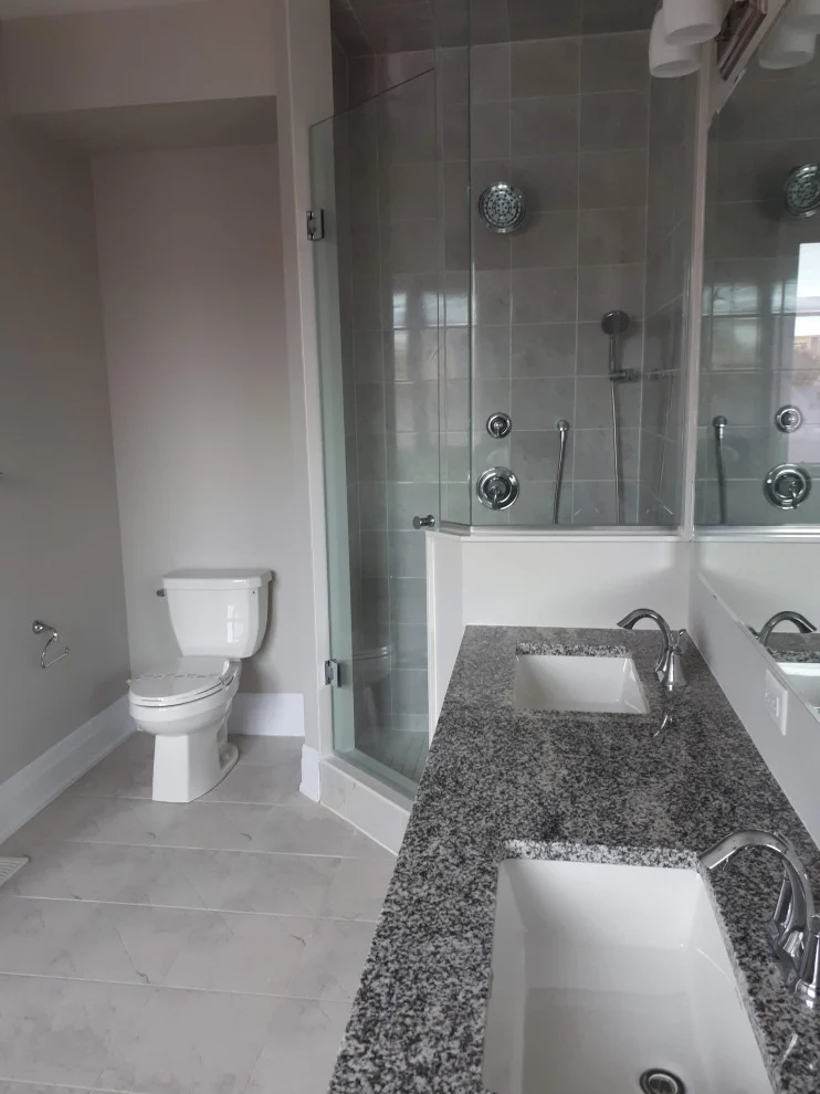 Granite vanity with undermount sink beside glass shower with multiple body jets and toilet