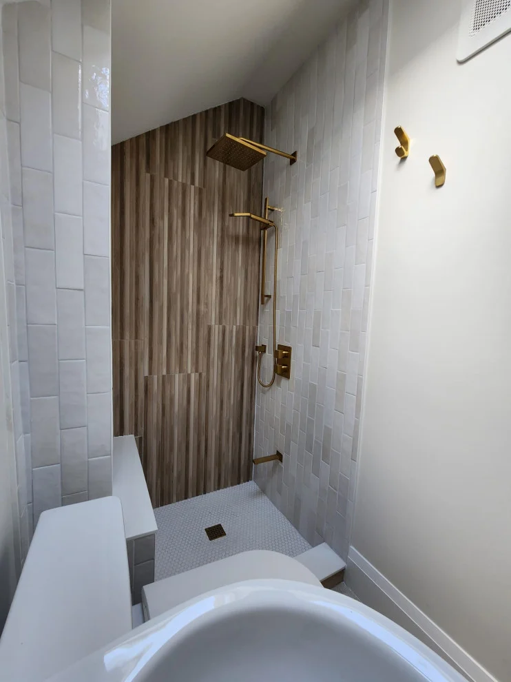 Shower under sloped ceiling with wood-grain tile wall, white tile and brushed gold rain head