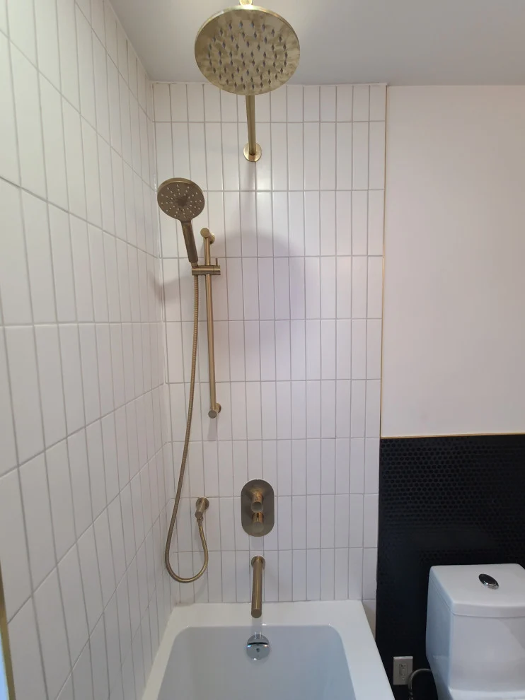 Brushed gold rain shower head and handheld shower on white vertical tile above tub