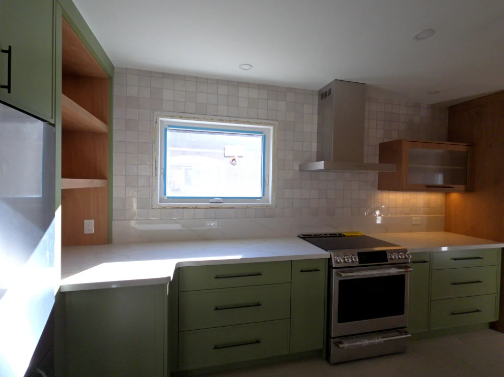 Green kitchen with stainless range, chimney hood, white tile backsplash and window over counter