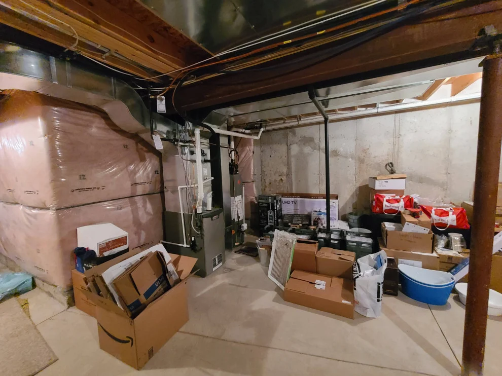 Unfinished basement with exposed joists, insulation, ductwork and stored boxes before renovation