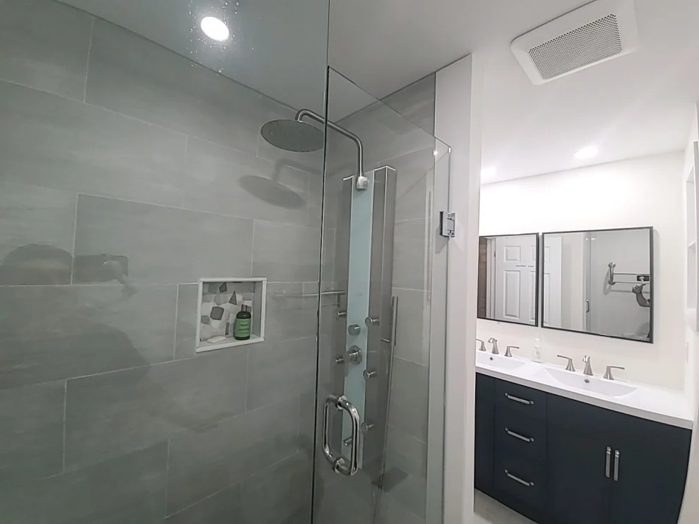 Grey tiled glass shower with shower panel and niche, navy double vanity in background