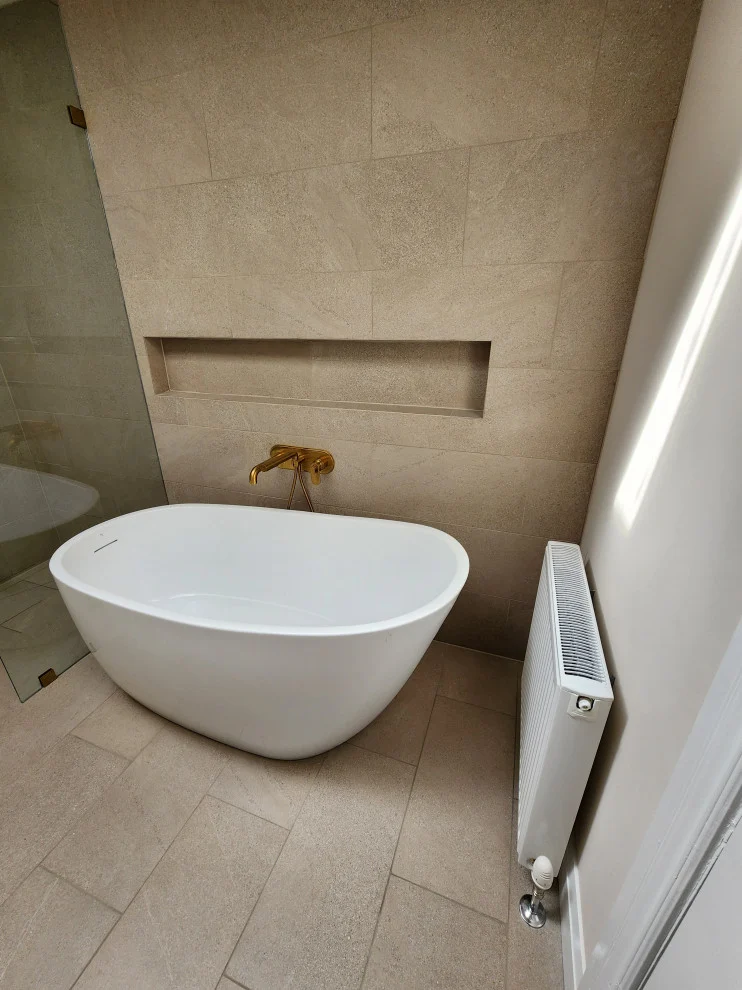 Freestanding white tub with wall-mounted gold faucet, long niche and white panel radiator